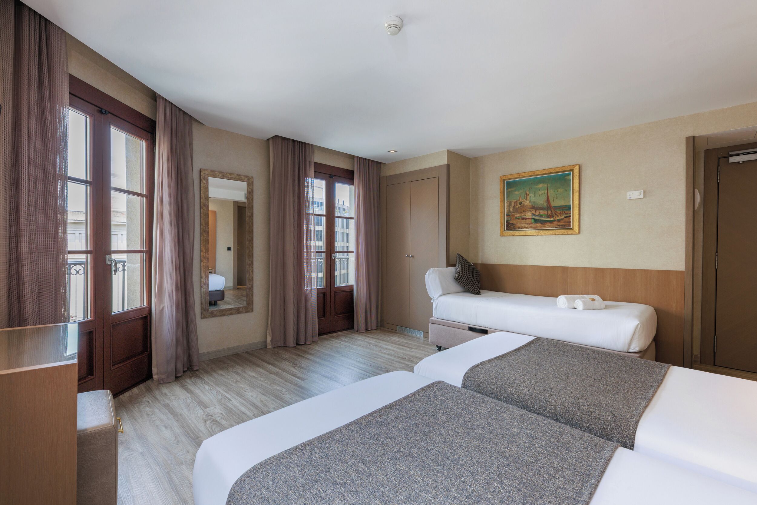Una habitación de hotel con dos camas, un armario de madera, un espejo grande y un cuadro en la pared.