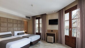 A hotel room with two beds, a flat-screen TV, a small table, and a window with curtains. - Hotel Suizo (Barcelona)
