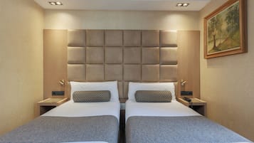 Habitación de hotel con dos camas, un cabecero grande y acolchado, mesitas de noche con lámparas y un cuadro en la pared.