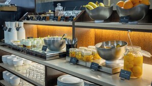 A buffet with various food items and beverages, including bowls of fruit and containers of condiments. - Hotel Suizo (Barcelona)