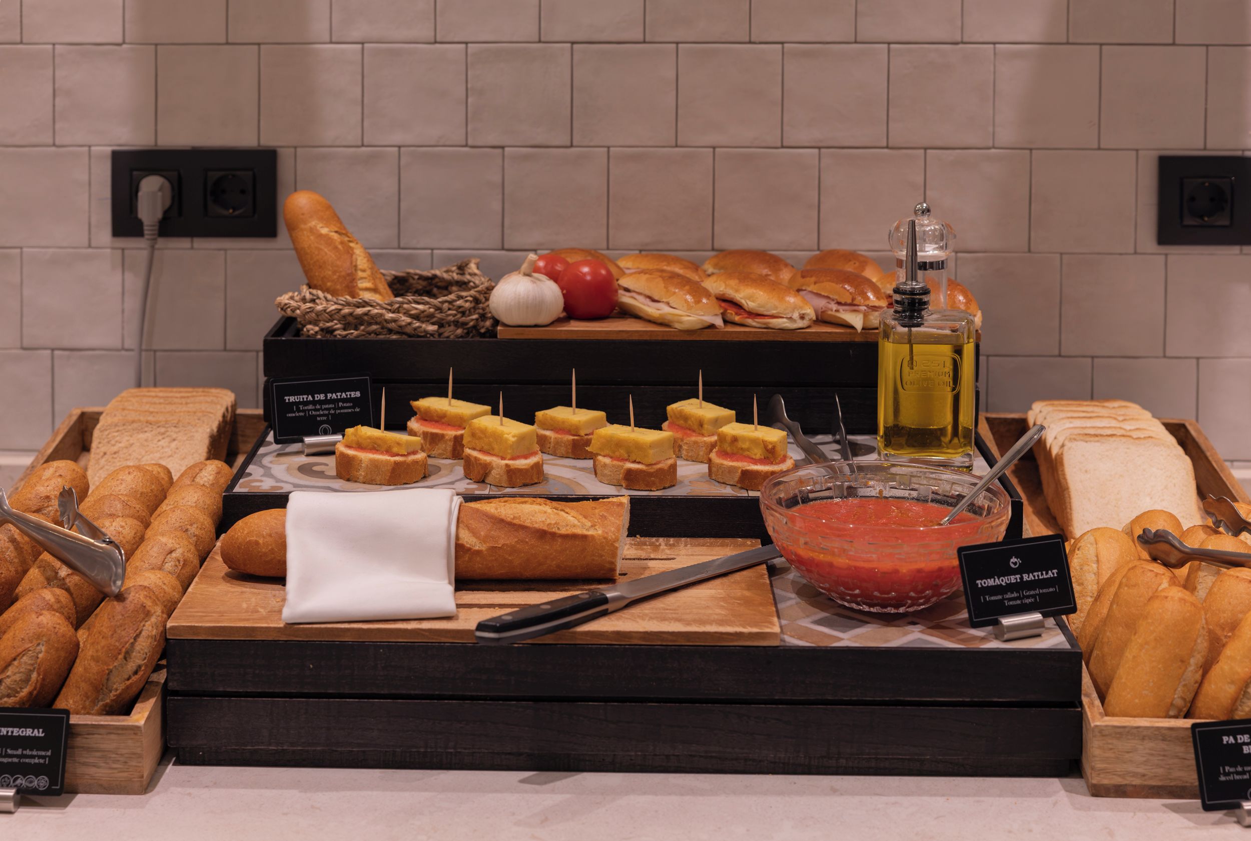 Una mesa de buffet con panes variados, un tazón de salsa de tomate y una botella de aceite de oliva.