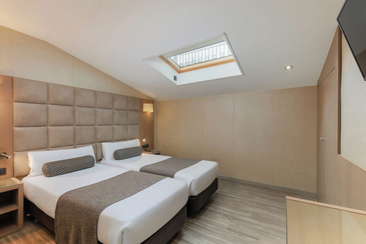 Ein modernes Hotelzimmer mit zwei Betten, einem Oberlicht und einem Holzboden.