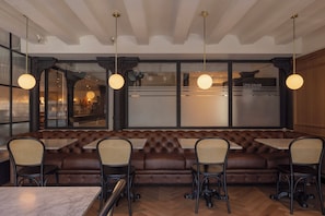 A restaurant interior with a long brown leather bench, four tables with chairs, and pendant lighting. - Hotel Suizo (Barcelona)