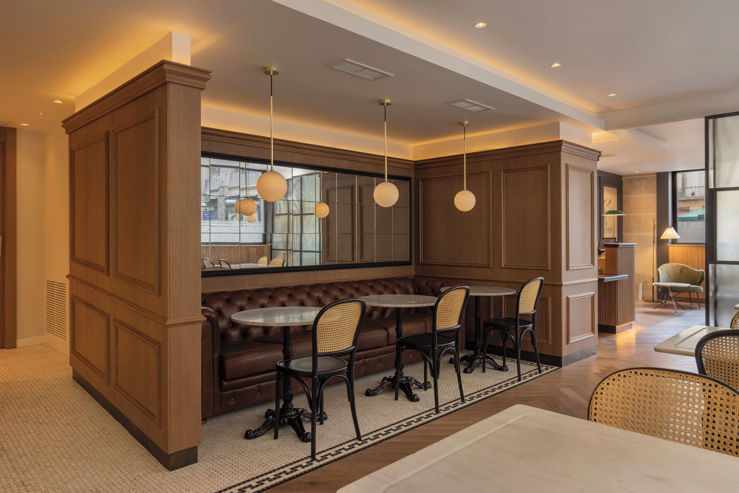 Un interior moderno con una zona de estar central que incluye un banco de cuero marrón y cuatro sillas, una mesa redonda e iluminación colgante.