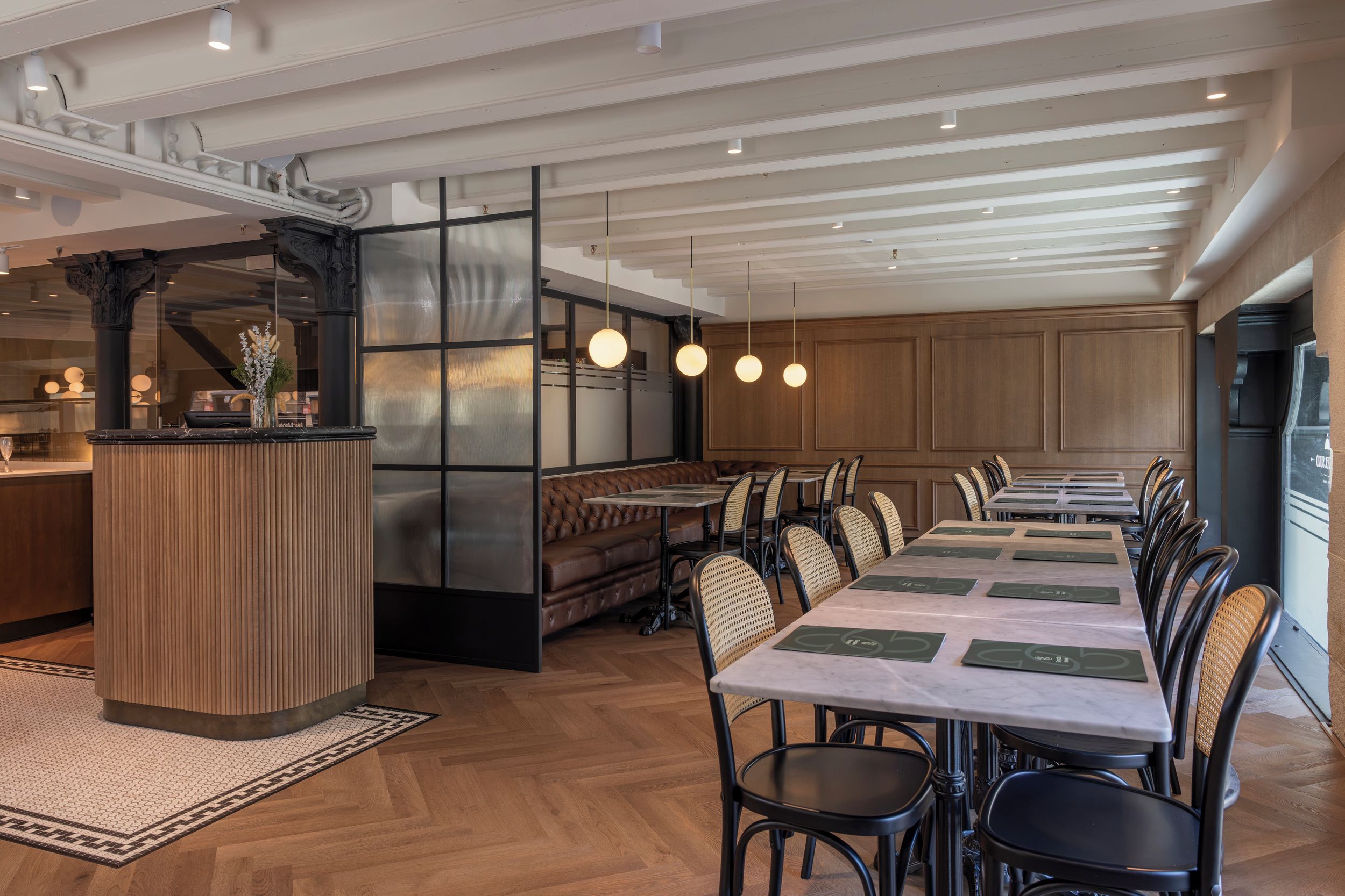 Uma sala de jantar moderna com uma mesa comprida, assentos acolchoados e iluminação pendente.