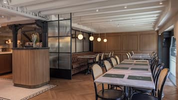 Uma sala de jantar moderna com uma mesa comprida, assentos acolchoados e iluminação pendente.