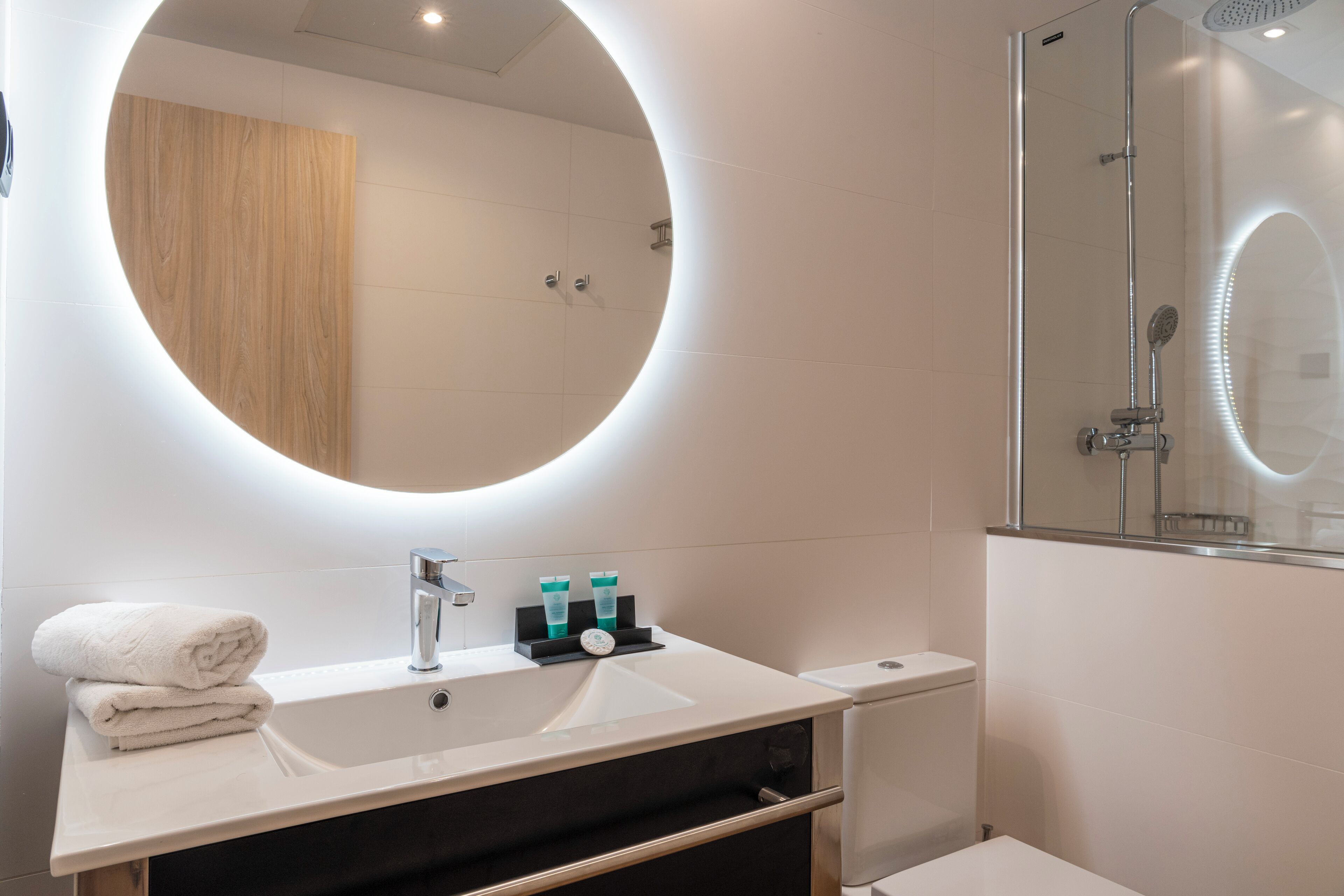 A modern bathroom with a round mirror, a sink, and a shower.