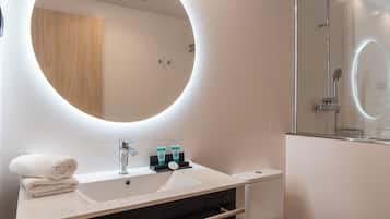 Un baño moderno con un espejo redondo, un lavamanos y una ducha.