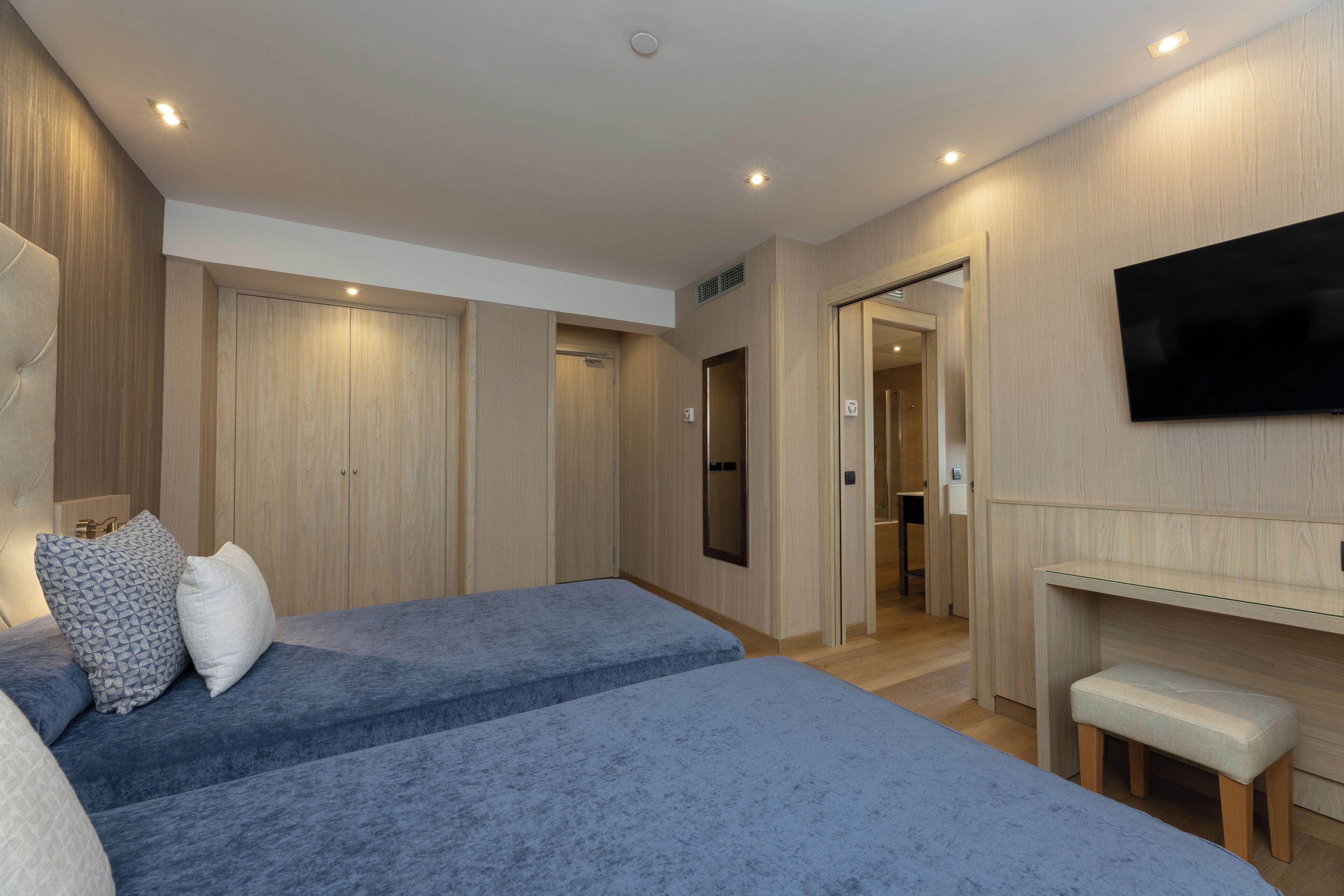 A modern hotel room with two beds, a flat-screen TV, and a desk.