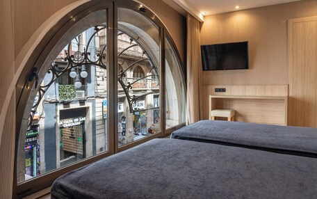 A hotel room with two beds, a large arched window, a mounted TV, and a small bedside table.