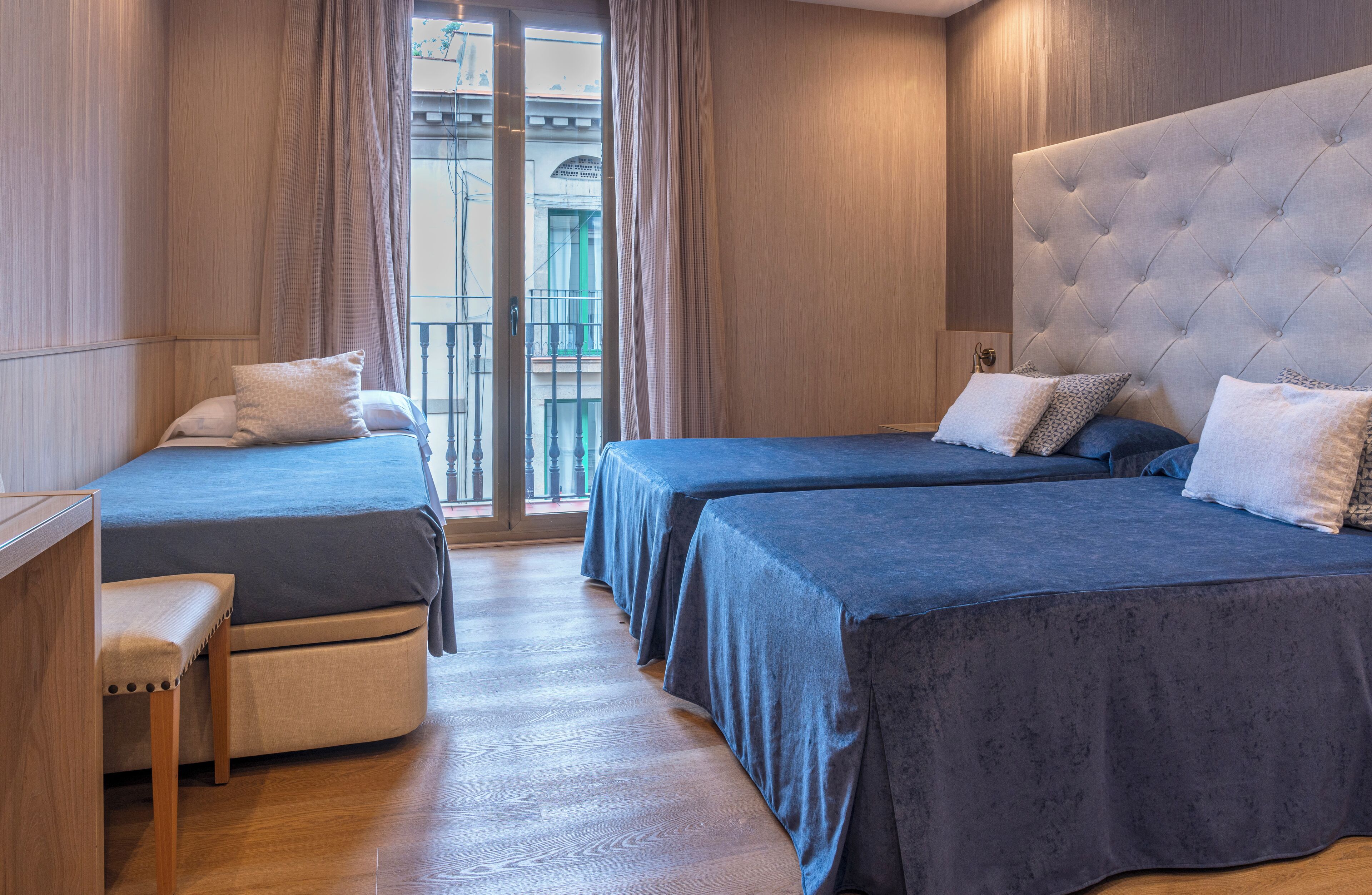 A hotel room with two beds, a bench, and a view of the outside.