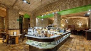 A breakfast buffet area with a central serving counter, multiple seating arrangements, and a brick wall backdrop. - Rialto (Barcelona)