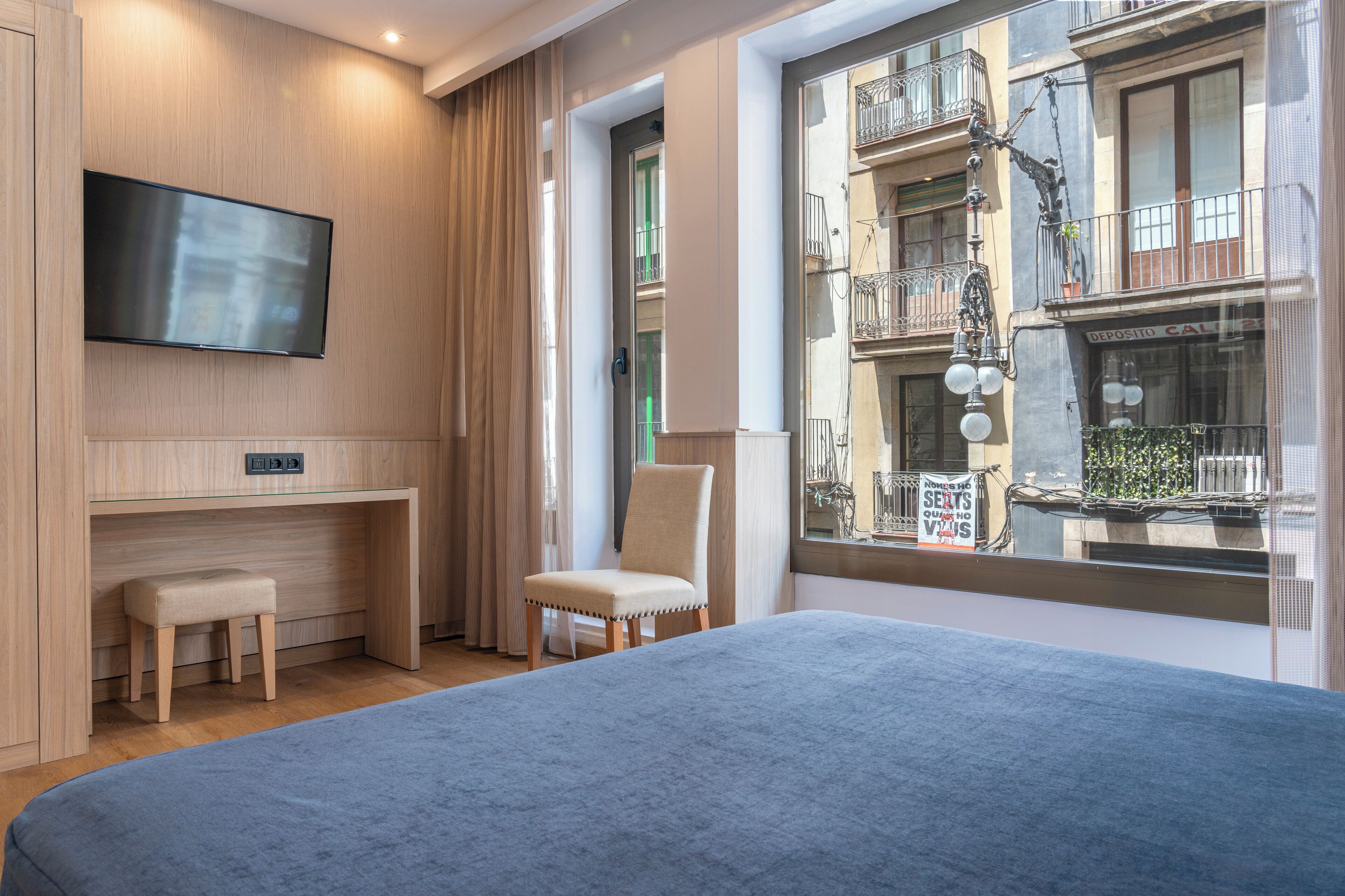 A modern hotel room with a large bed, a desk, a chair, and a TV mounted on the wall.