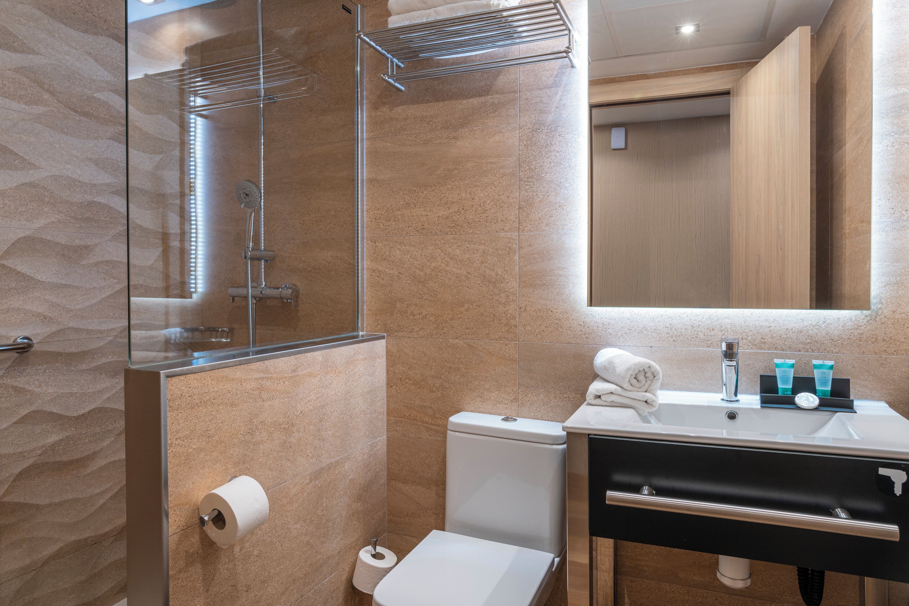 A modern bathroom with a glass shower enclosure, a toilet, and a sink with toiletries.