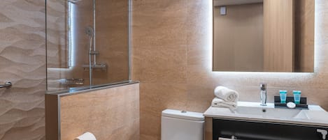 A modern bathroom with a glass shower enclosure, a toilet, and a sink with toiletries.