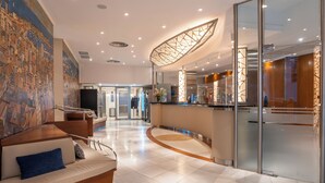 A modern lobby with a curved reception desk, a seating area with a sofa, and a large abstract mural on the wall. - Rialto (Barcelona)