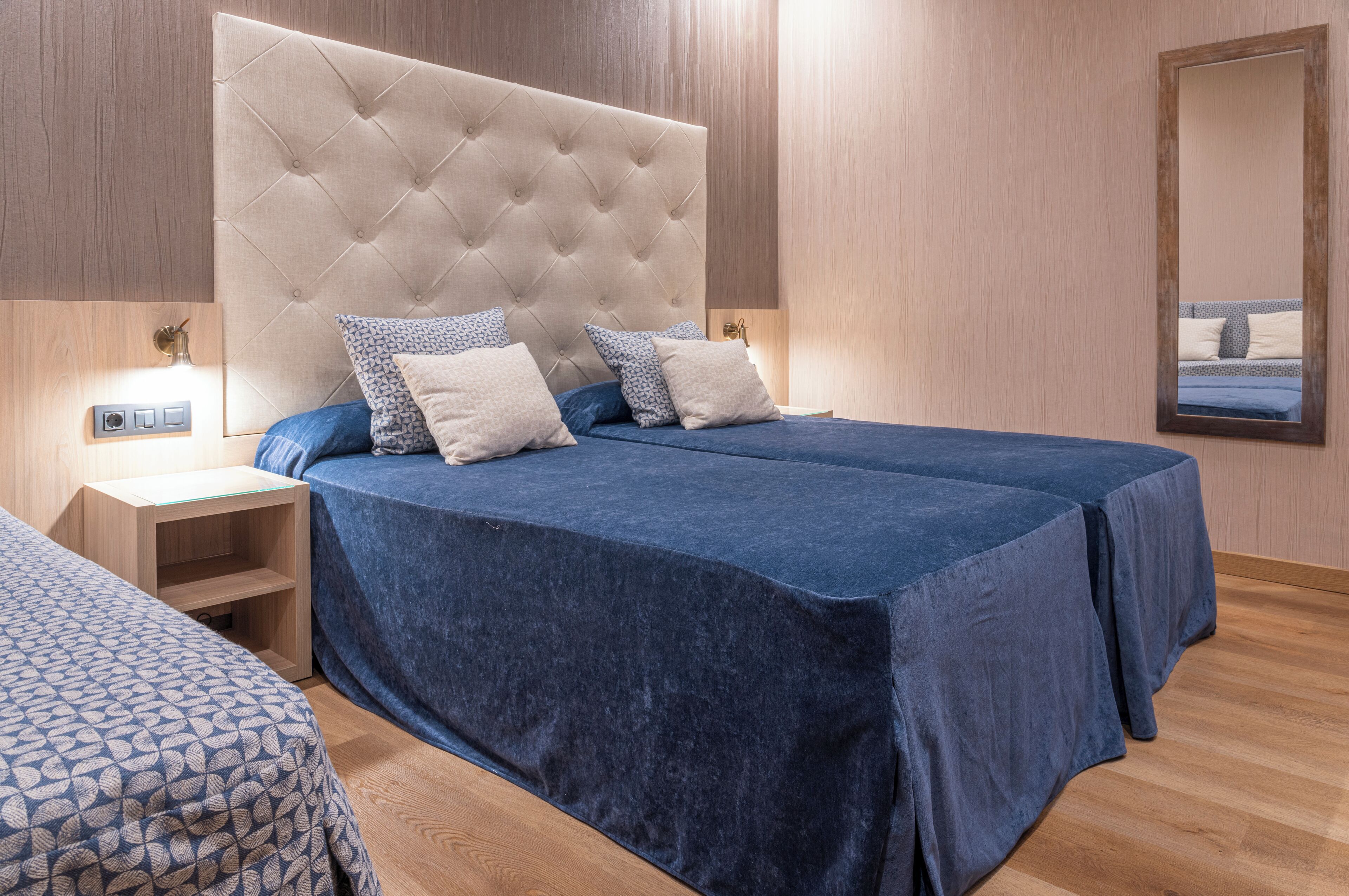 Un lit double avec une tête de lit capitonnée, deux tables de chevet et une petite table de nuit avec une lampe.