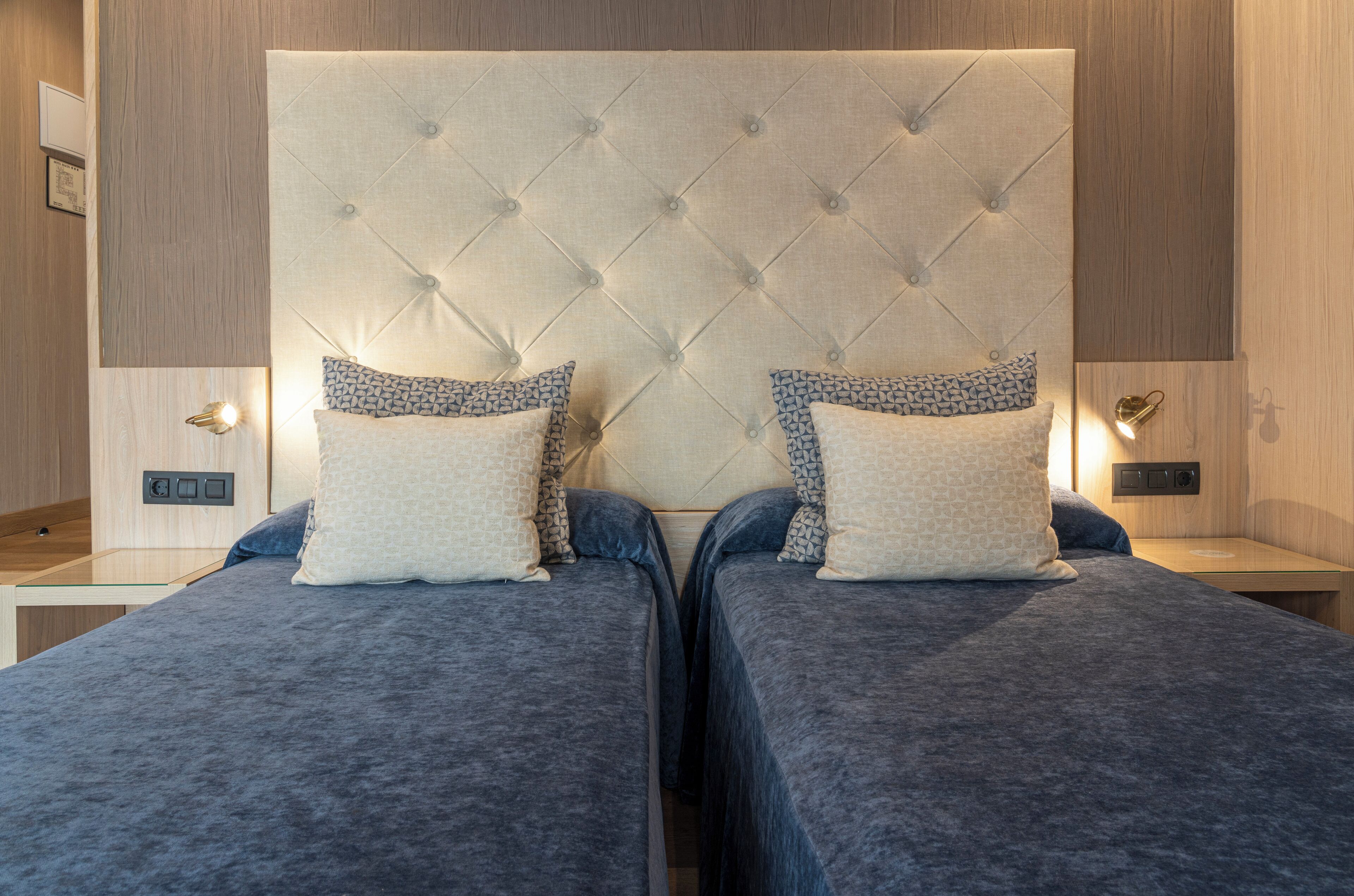 Cama doble con cabecera capitonada, dos mesitas de noche y almohadas estampadas.