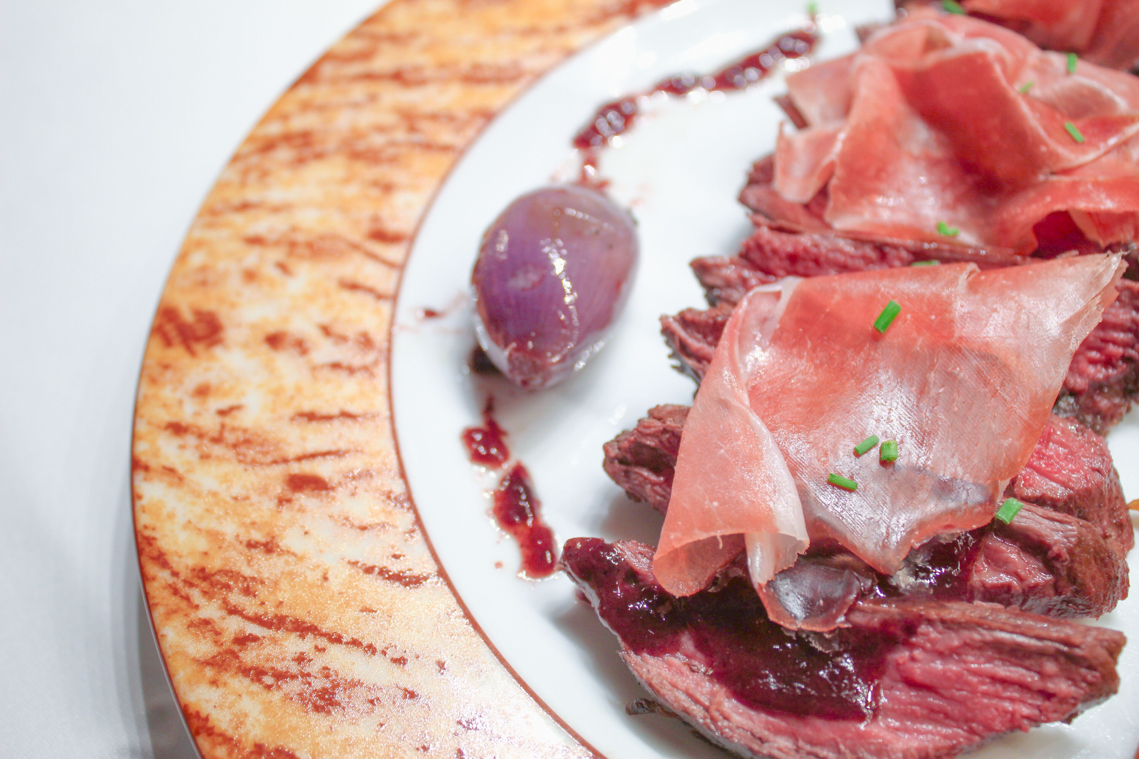 Um prato com carne fatiada, molho vermelho e um pequeno objeto roxo.
