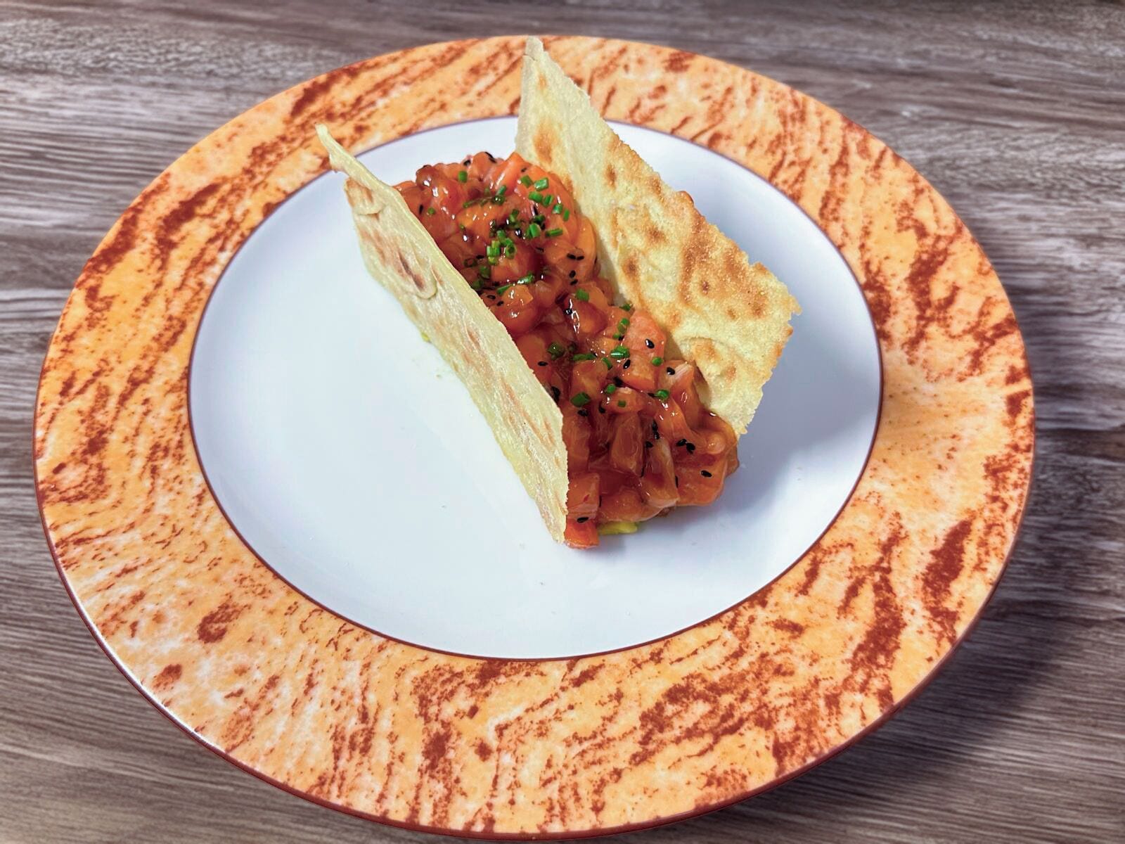 A plate with a tortilla wrap filled with a tomato-based dish, garnished with green herbs, on a white plate with a patterned rim.