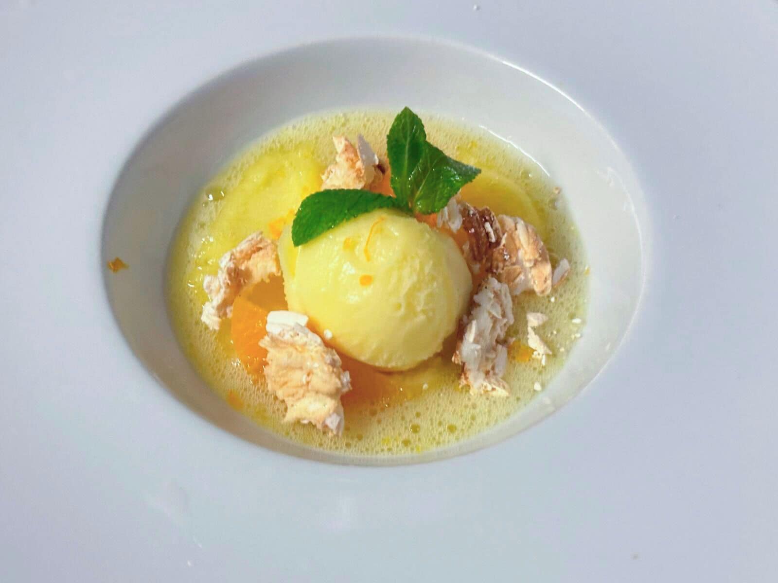 Postre con una porción de helado, adornado con una hoja de menta, servido en un tazón blanco.