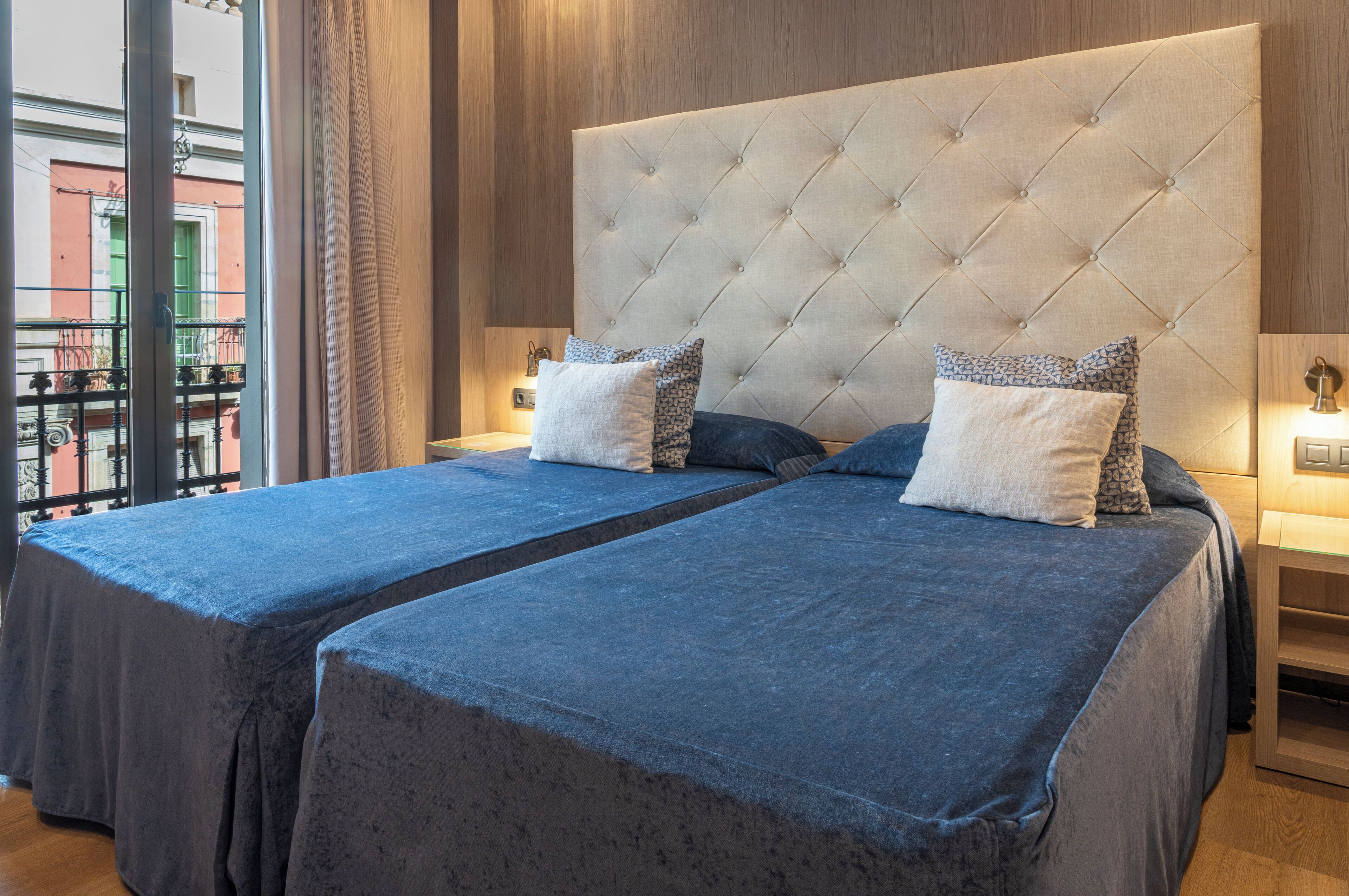 A hotel room with two beds, a large tufted headboard, and a balcony view.