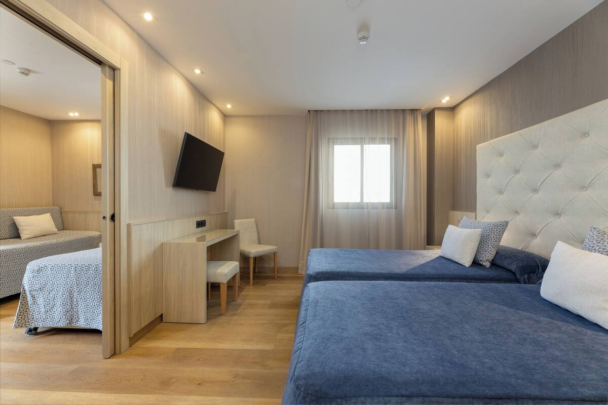A modern hotel room with two beds, a desk, and a TV.