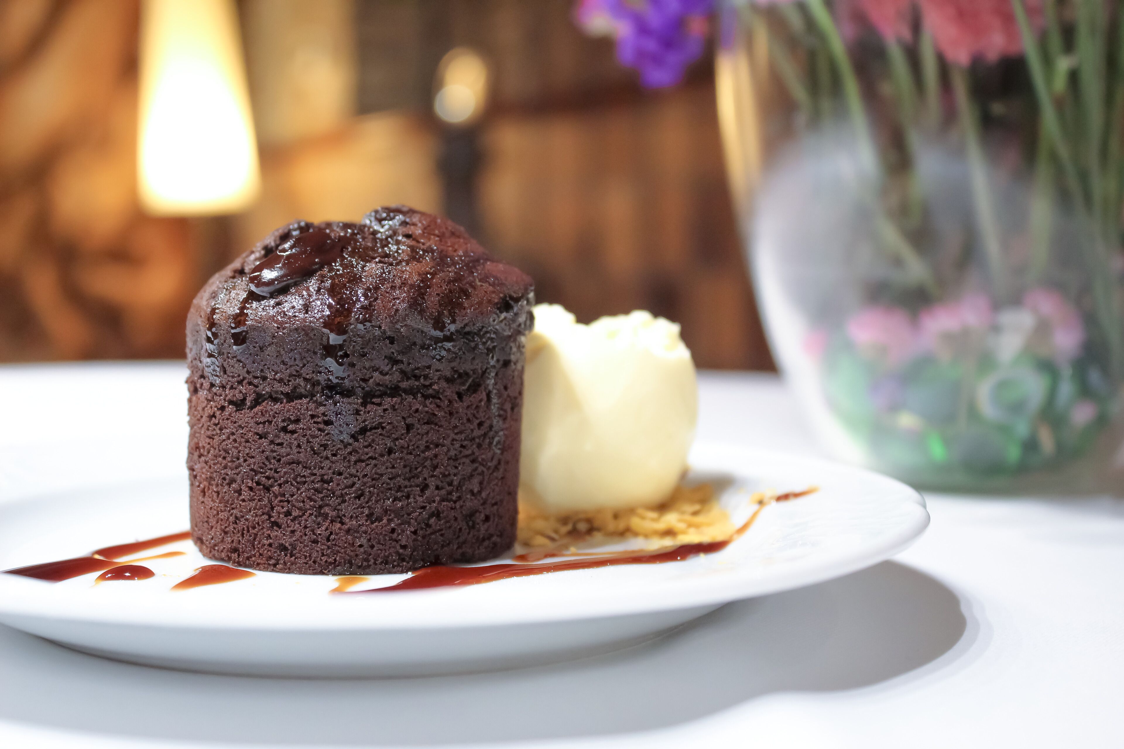 A dessert on a white plate with a chocolate cake and a scoop of vanilla ice cream, accompanied by a drizzle of chocolate sauce.