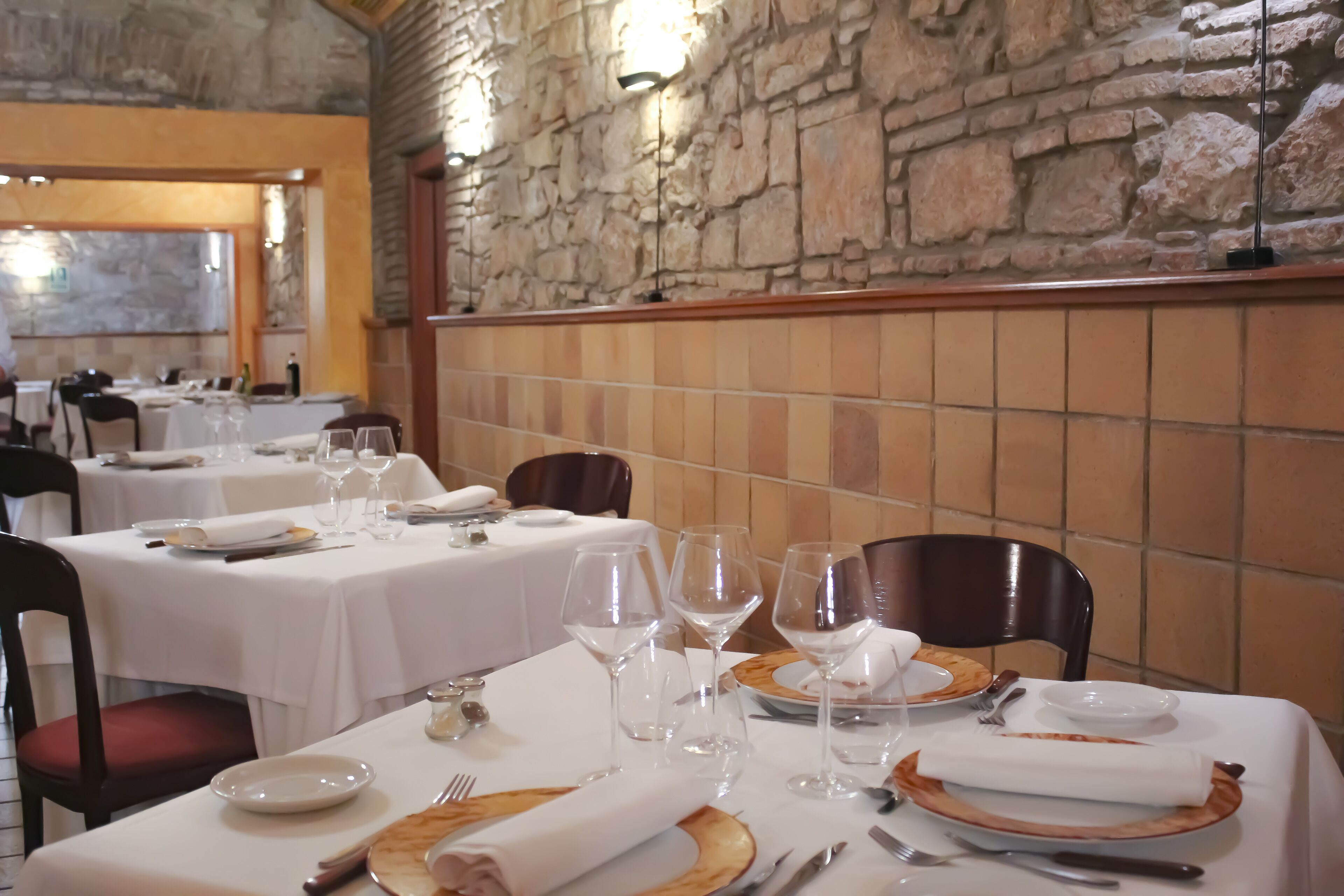 Un restaurante con mesas dispuestas para comer, paredes de piedra y vistas a través de una ventana.