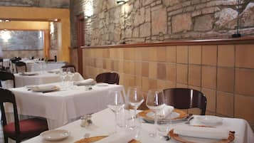 Un restaurante con mesas dispuestas para comer, paredes de piedra y vistas a través de una ventana.