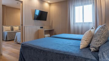 A hotel room with two beds, a TV mounted on the wall, and a window with curtains.