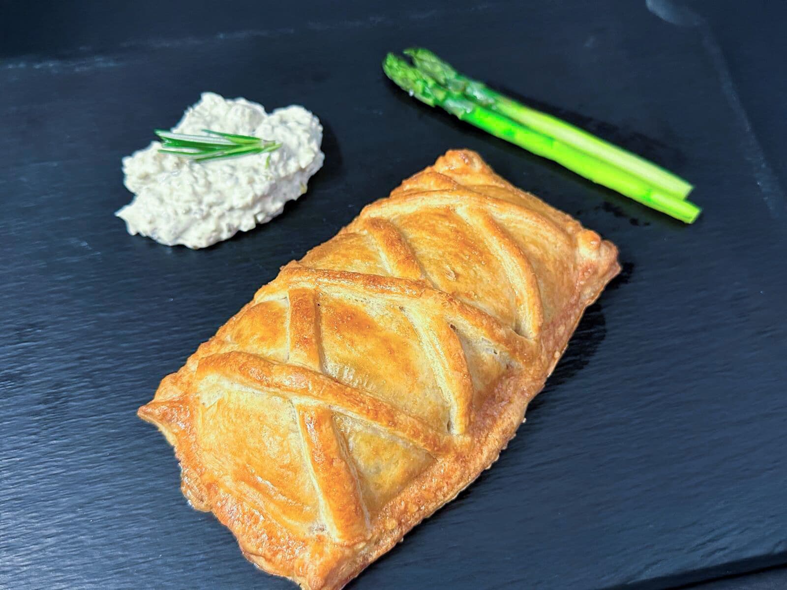 Un pasticcino su un piatto in ardesia, accompagnato da una salsa cremosa e asparagi.