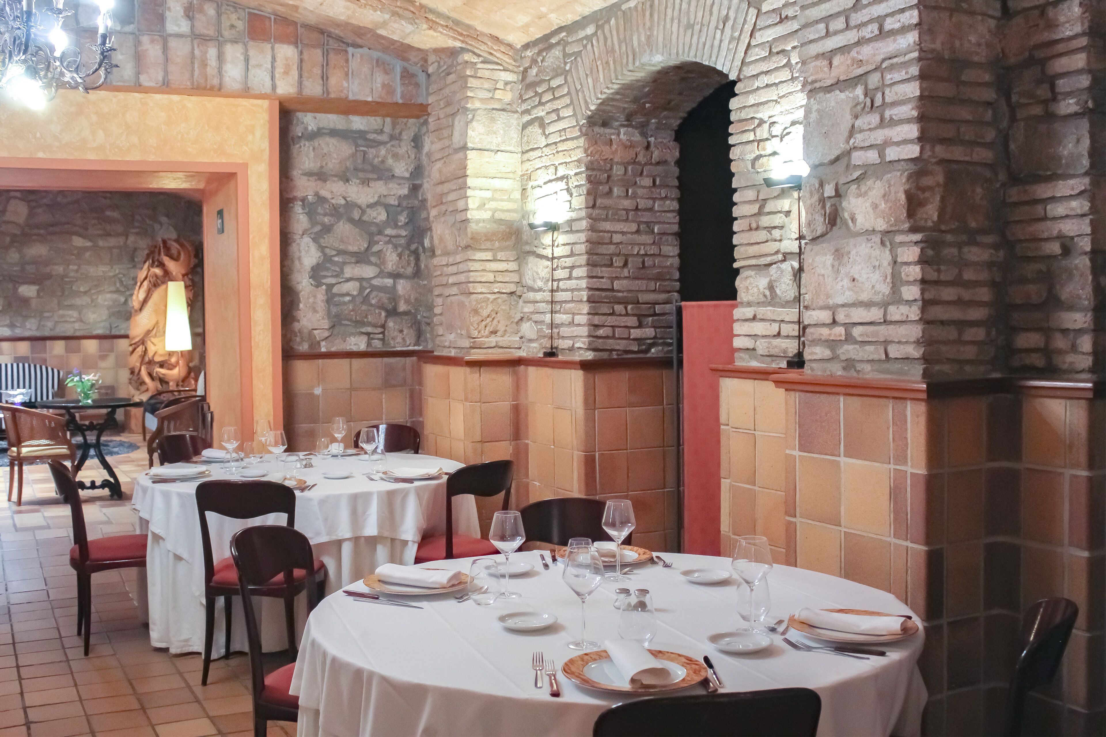A restaurant with stone walls and white tablecloths. Tables are set with plates, glasses, and cutlery.