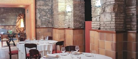 A restaurant with stone walls and white tablecloths. Tables are set with plates, glasses, and cutlery.