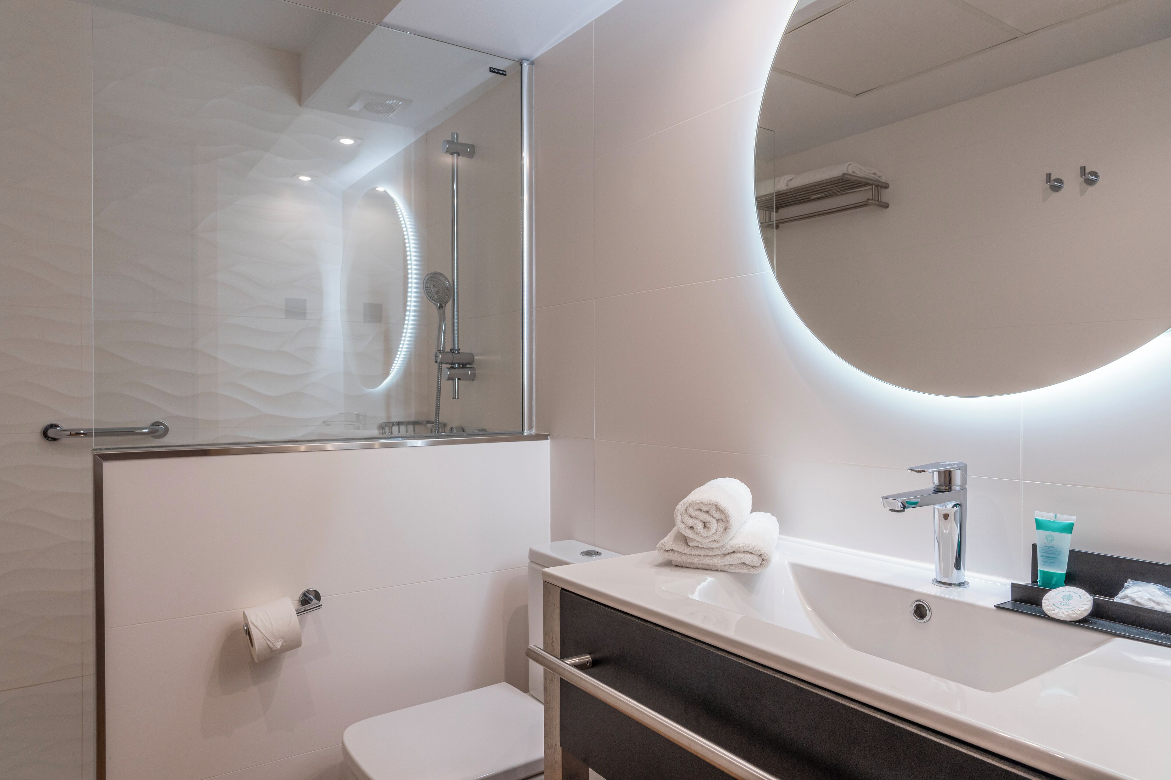 A modern bathroom with a glass shower enclosure, a white toilet, a vanity with a mirror, and a sink.