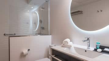 Ein modernes Badezimmer mit Duschkabine aus Glas, Toilette in Weiß, Waschtisch mit Spiegel und Waschbecken.