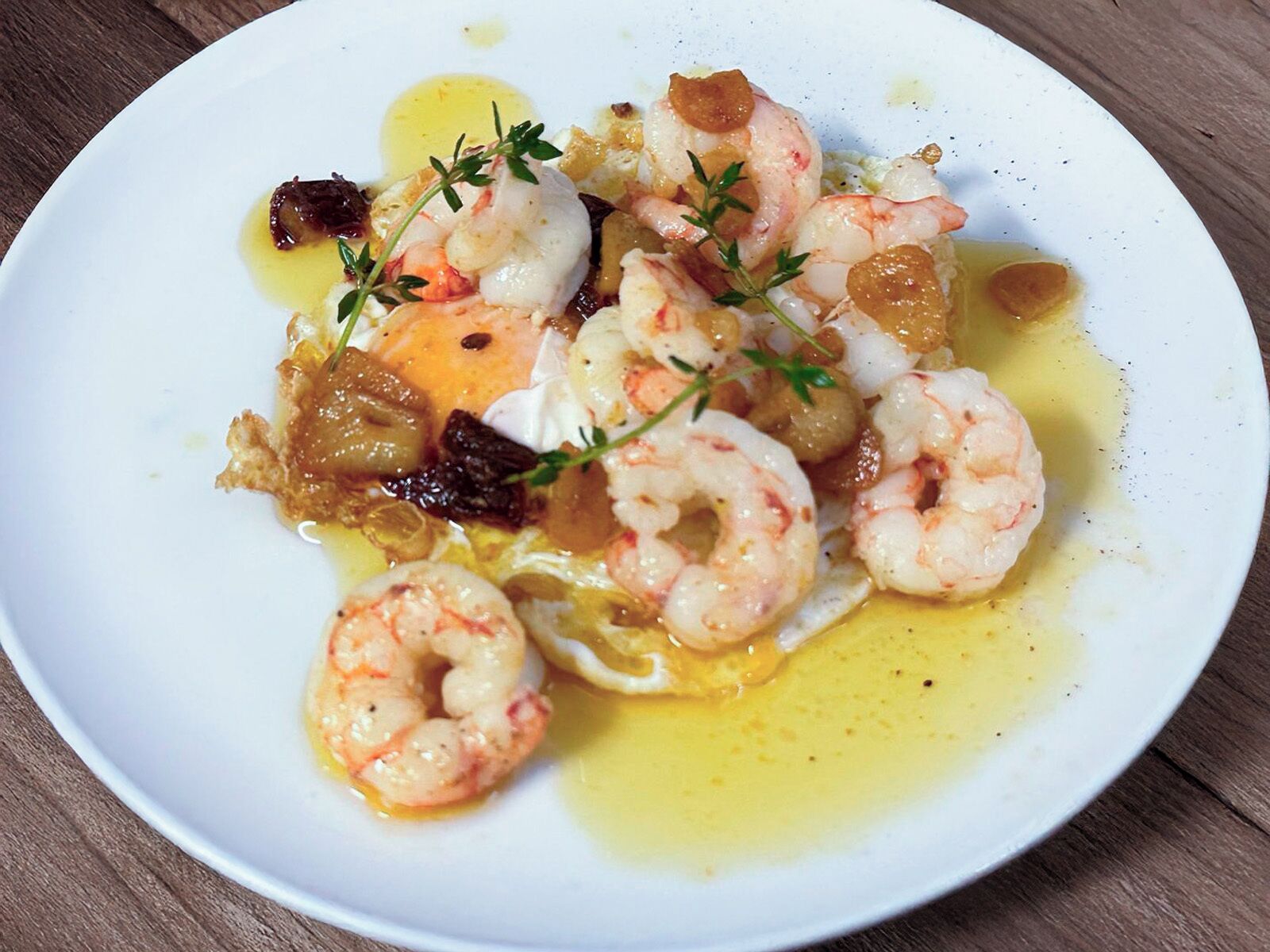 A plate of cooked shrimp with herbs and a sauce.