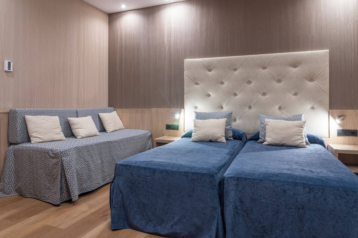 A hotel room with two beds, a sofa, and a nightstand.