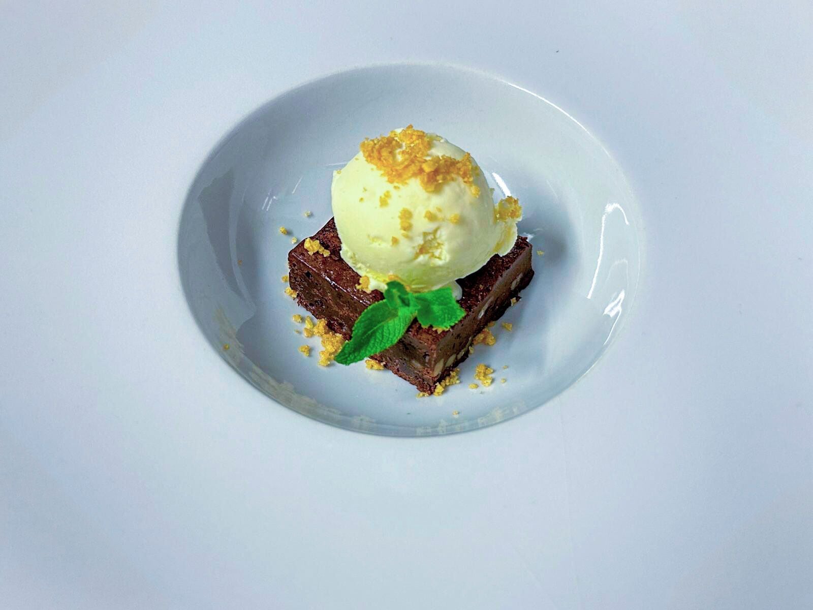 A dessert consisting of a scoop of ice cream on top of a piece of cake, garnished with crumbled topping and a mint leaf.