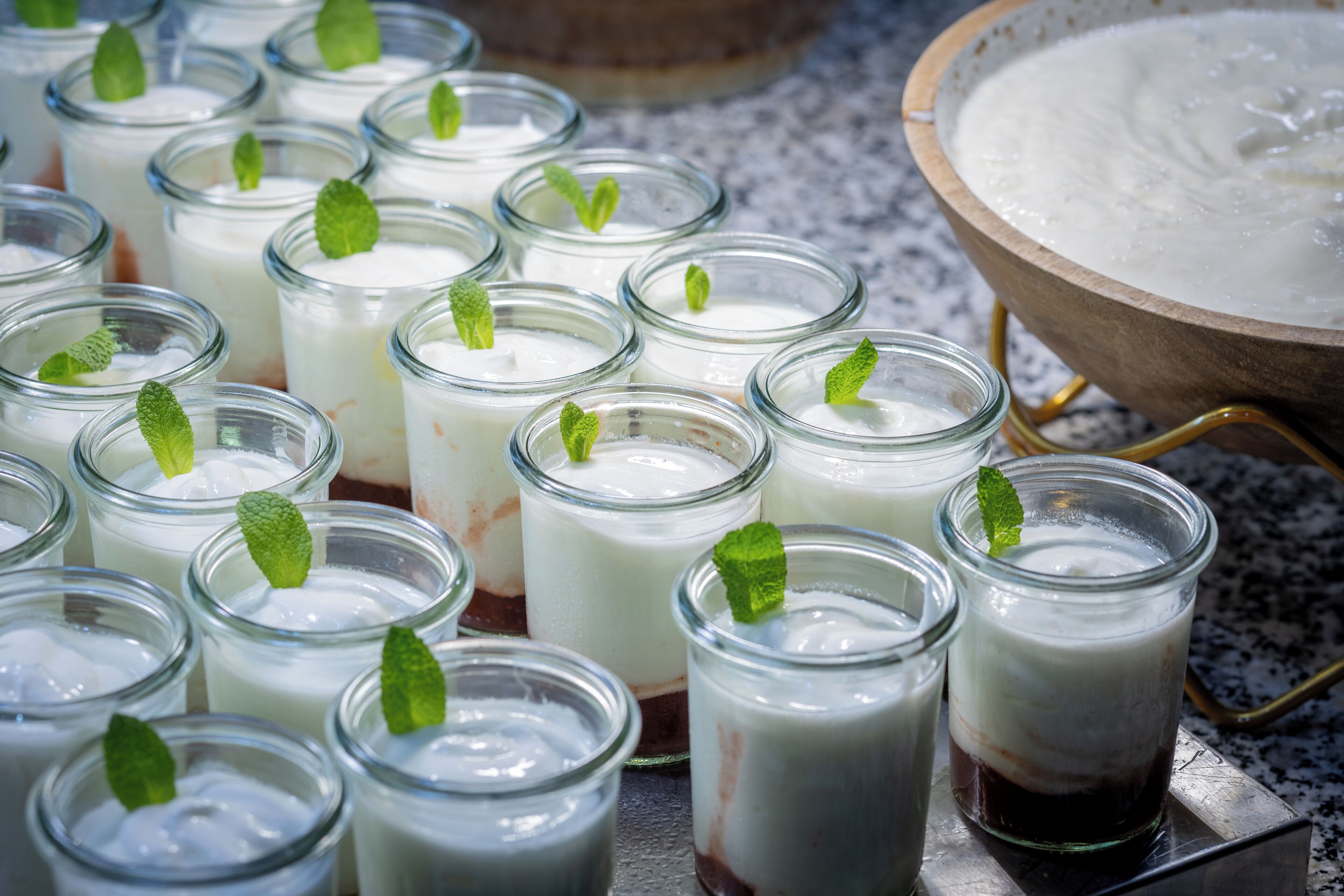 A variety of glass jars containing a white creamy substance, some garnished with mint leaves, arranged on a metal surface.