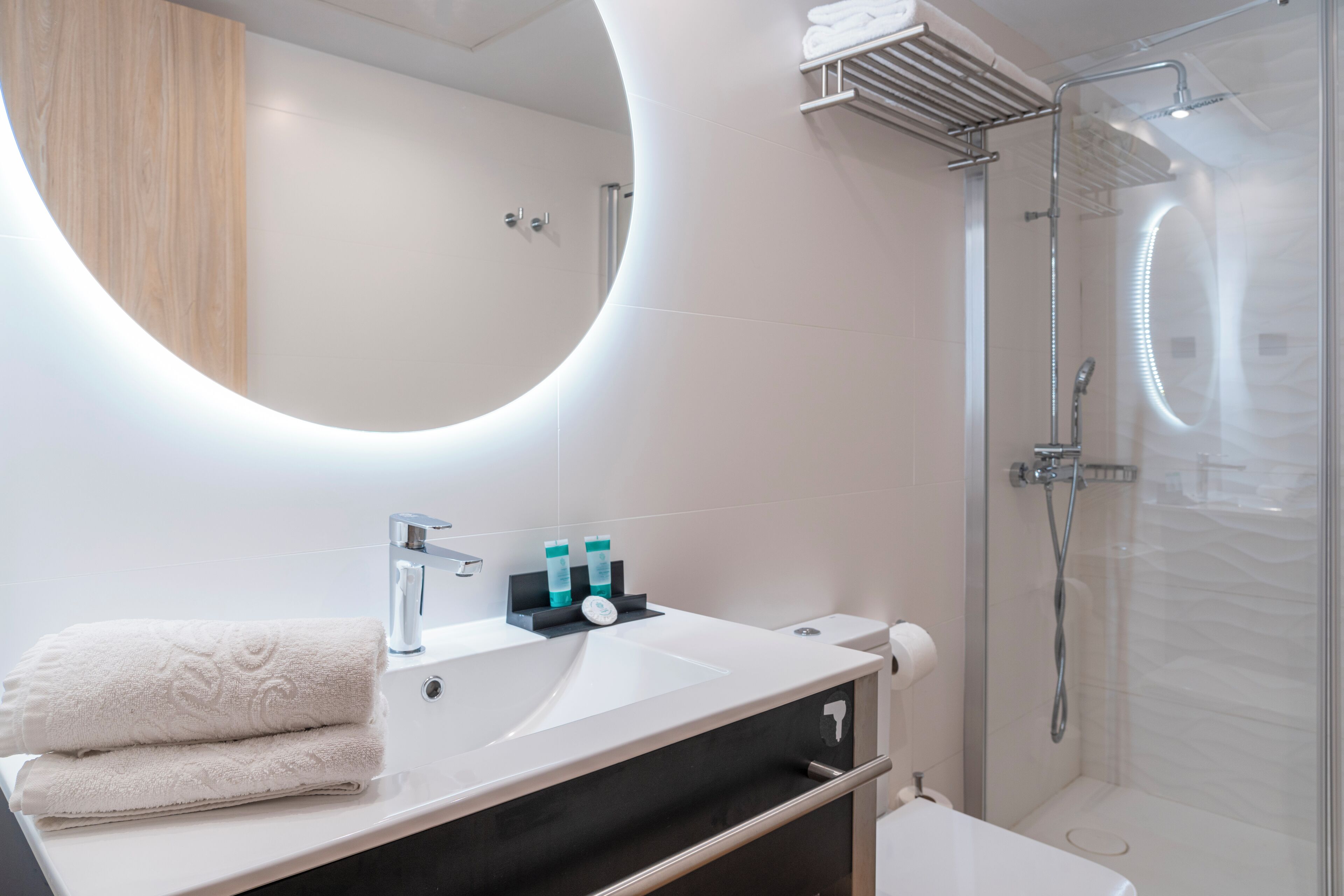 Une salle de bain moderne avec un grand miroir rond, un lavabo et une douche.