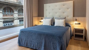 Una habitación de hotel moderna con una cama grande, dos mesitas de noche y vistas a un edificio con la palabra 'SPAIN' en la ventana.