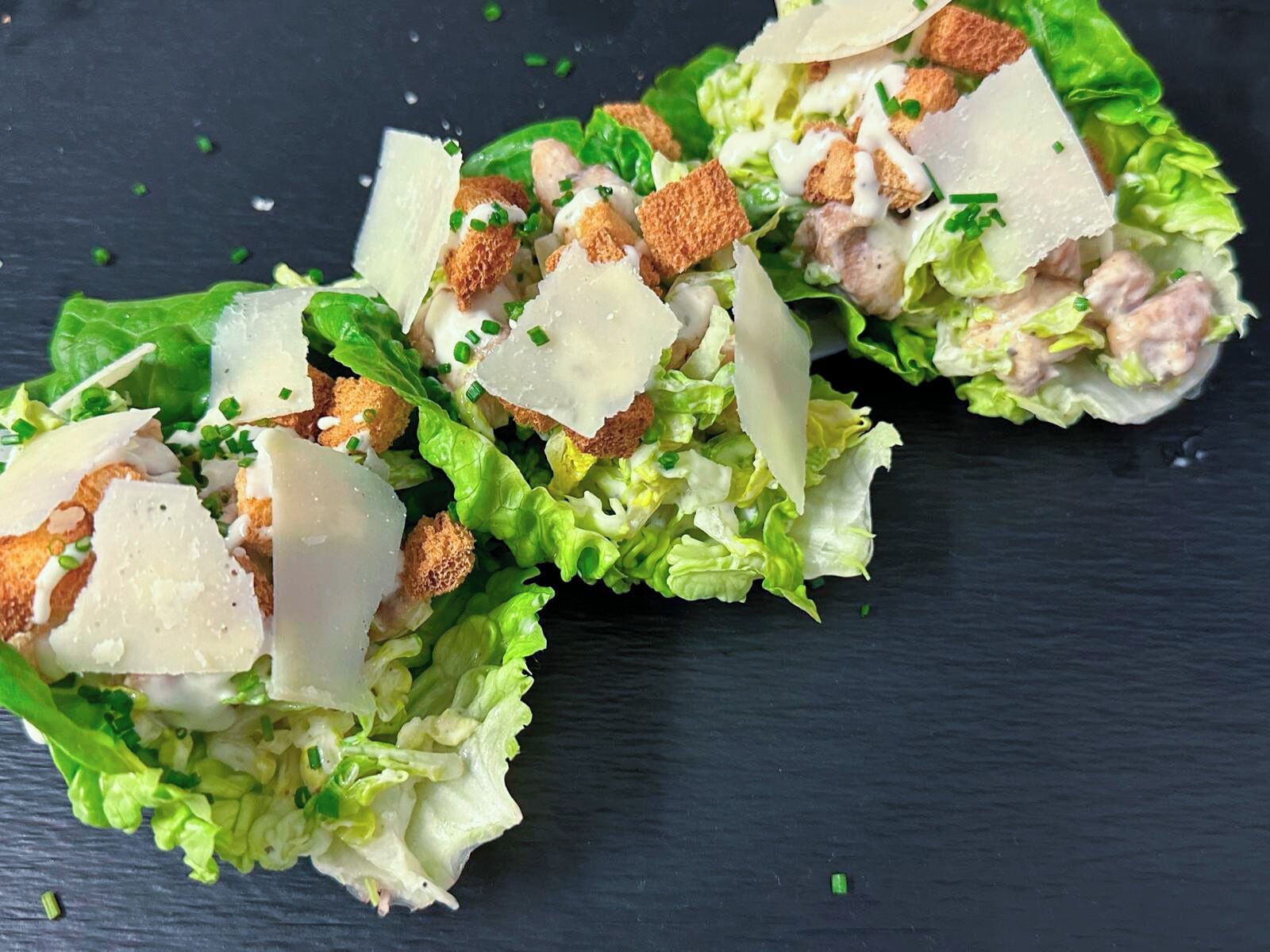 Een salade met sla, croutons en kaas op een donker oppervlak.