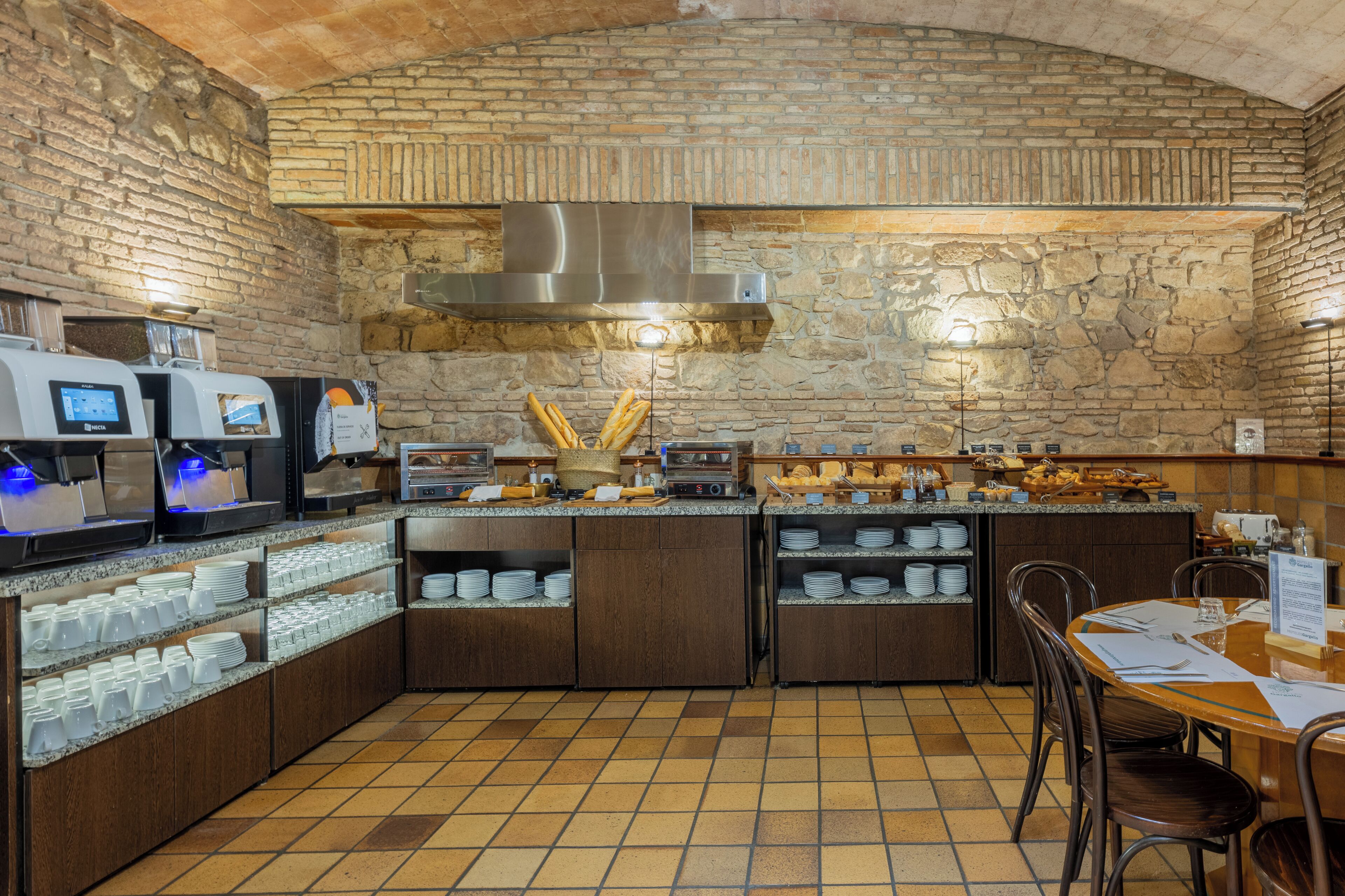 A breakfast bar with coffee machines, a stone wall, and a tiled floor.