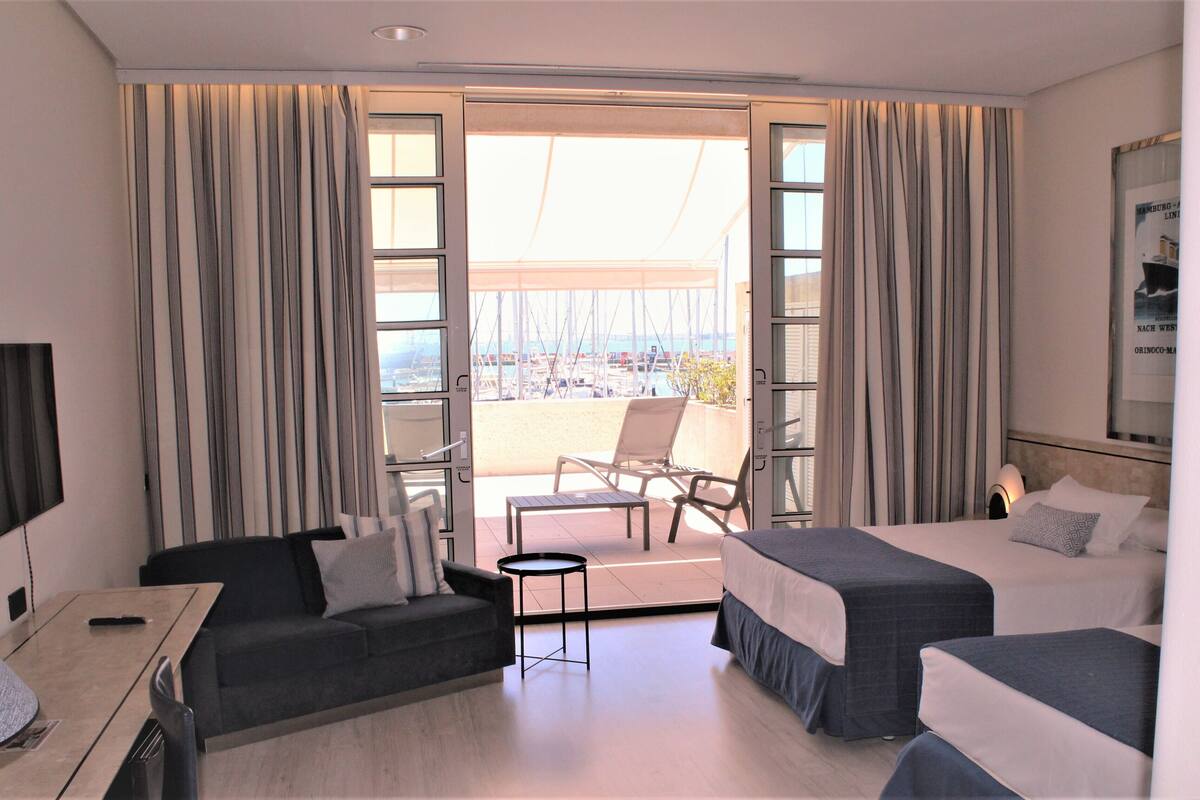Una habitación de hotel con balcón, un sofá, una cama y una mesita.