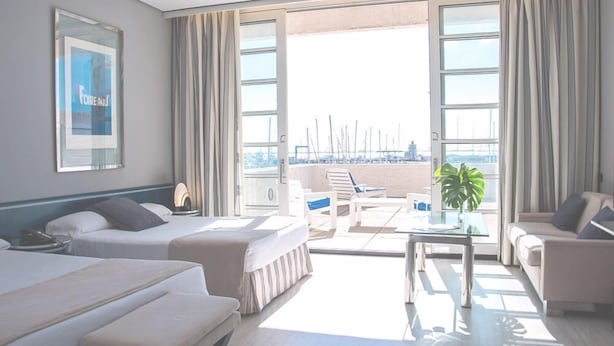 Une chambre d’hôtel avec deux lits, un balcon donnant sur le port de plaisance et un coin salon avec une table et des chaises.