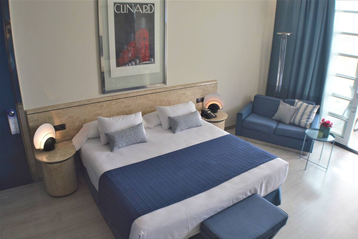 Habitación de hotel moderna con una cama grande, un sofá, una mesita y un cartel en la pared.