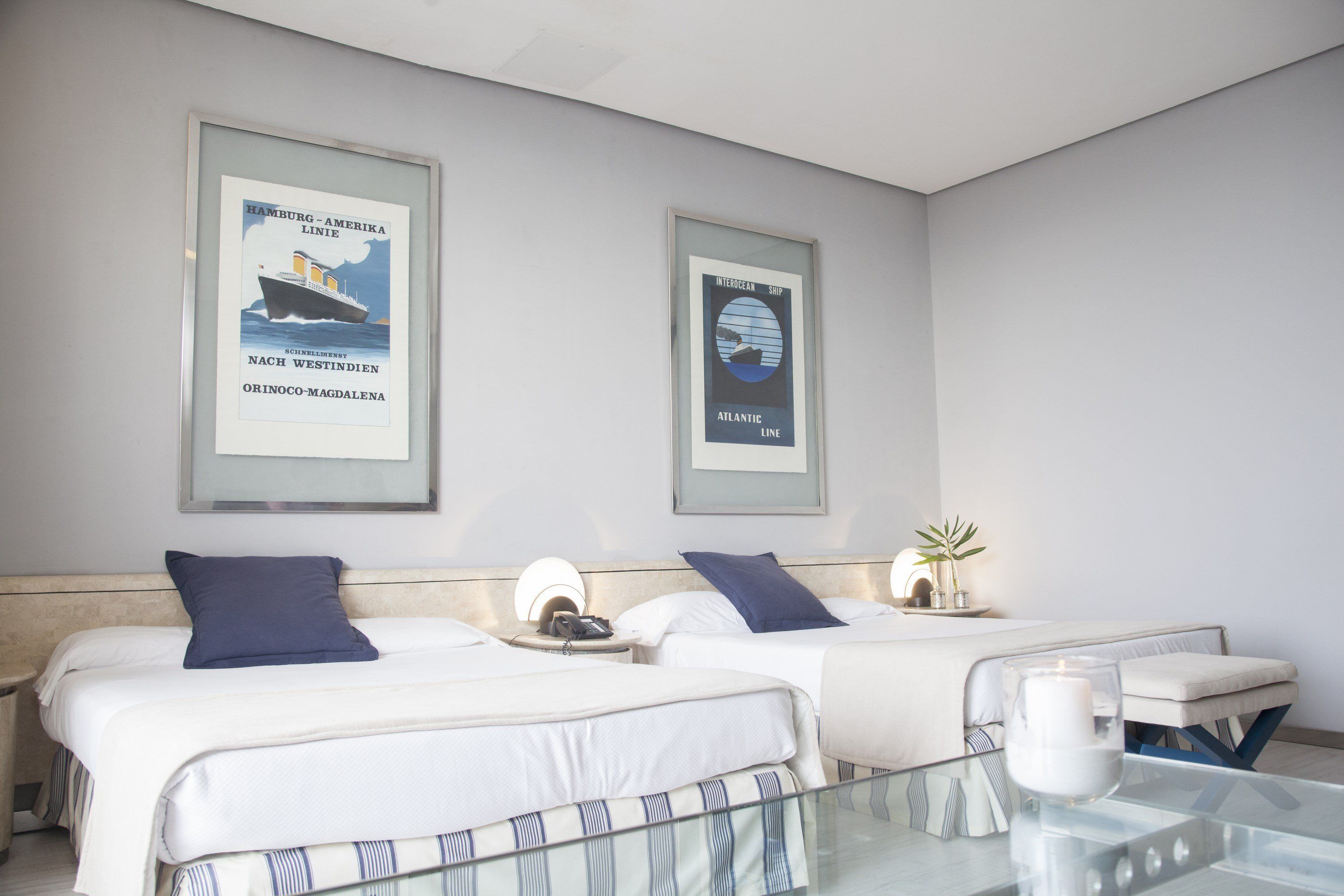 Ein Hotelzimmer mit zwei Betten, einem Glastisch und gerahmten Postern an der Wand.