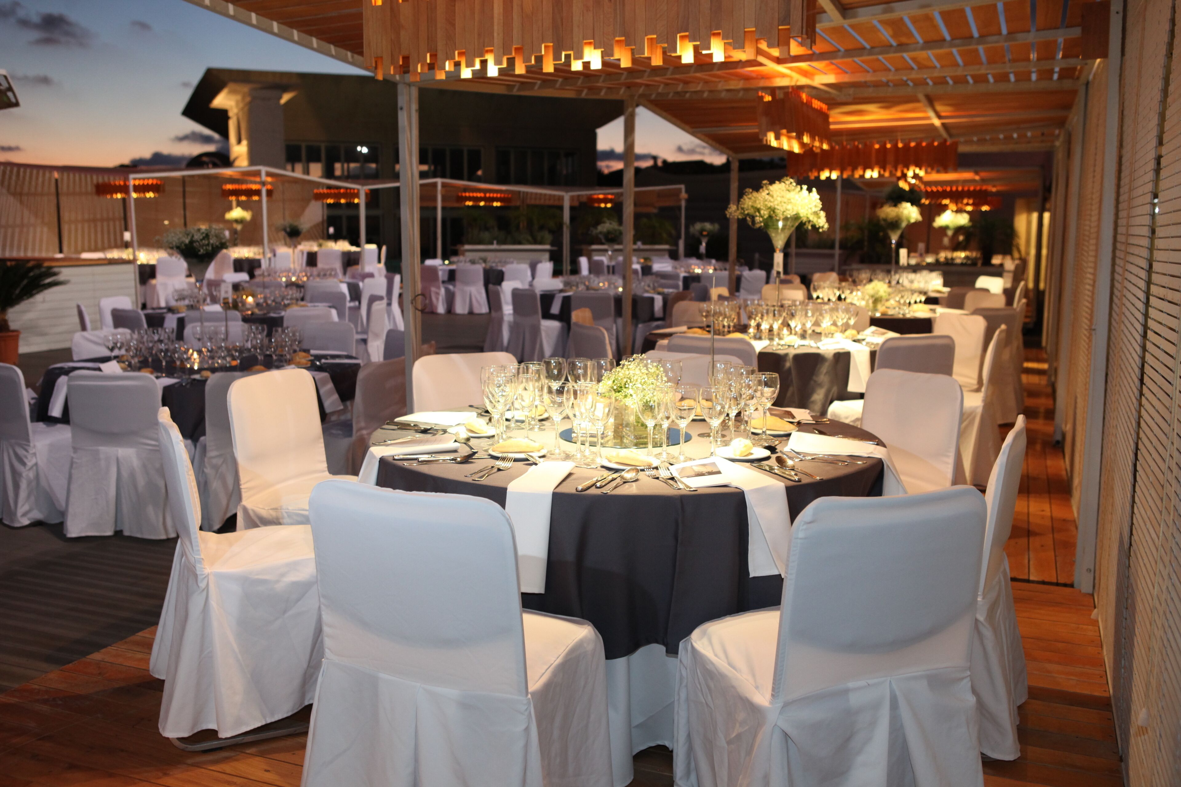 An outdoor dining area with round tables, white chairs, and a covered section with a wooden ceiling.