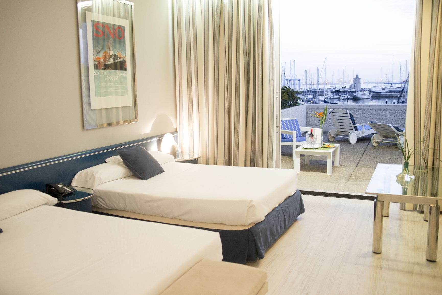 A hotel room with two beds, a small table, and a view of a marina.